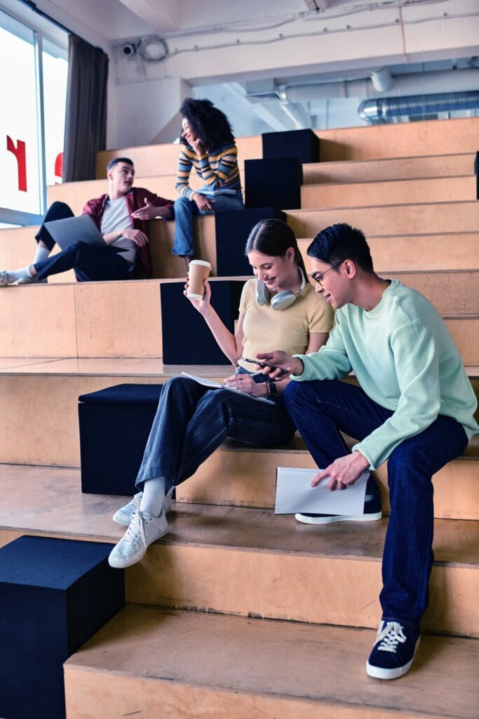 Multicultural group of students sitting atop stairs, engaged in conversation and contemplation